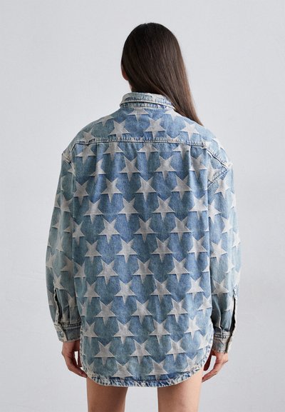 Denim oversize srajca s starim vzorcem v beli barvi na svetlom modrem ozadju, z dolgimi rokavi in klasičnim ovratnikom.