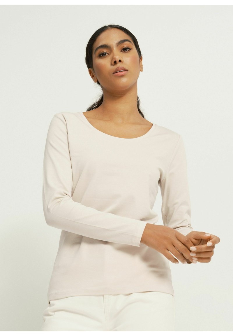Jasno beżowa bluzka z długim rękawem i okrągłym dekoltem, uszyta z miękkiego materiału, o dopasowanej sylwetce i gładkiej teksturze.