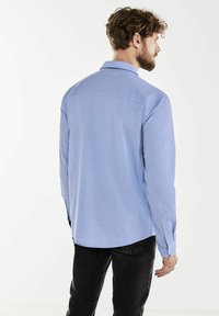 Světle modrá košile s dlouhým rukávem, s límečkem, zapínáním na knoflíky na manžetách a zakřiveným lemem, vyrobená z hladkého materiálu.