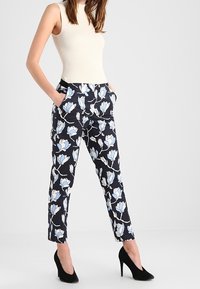 Kalhoty s květinovým potiskem v námořnické modři se světle modrými magnolovými vzory, vyrobené z lehkého materiálu. Obsahují boční kapsy a mají upravený střih.