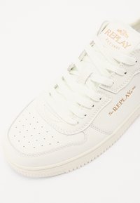 Hvide lædersneakers med perforerede detaljer, glat overflade, flade snørebånd og guld "REPLAY" branding på sidepanelet og tungen.