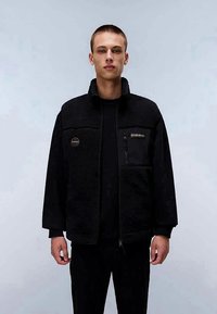 Parka preta de fleece com gola alta, fecho éclair frontal e bolsos. Apresenta uma superfície texturizada e um pequeno logótipo no peito.