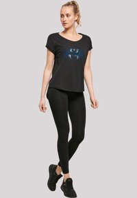 Svart t-skjorte med korte ermer med blå og grå grafisk design; parret med svarte leggings og svarte joggesko.