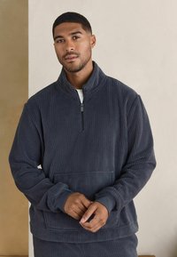 Dark gray pullover in a textured fabric with a mock collar, half-zipper, and front pocket; features ribbed cuffs and waist.