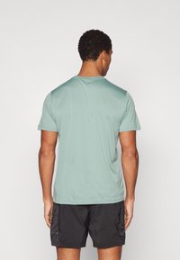 Camiseta atlética verde claro con mangas cortas, cuello redondo y una textura suave, combinada con pantalones cortos negros. Vista trasera.
