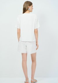 Top blanco de manga corta con acentos bordados, combinado con pantalones cortos blancos que presentan patrones florales y un dobladillo en forma de ondas. Textura suave, diseño casual.