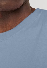 Camiseta de algodón azul claro con escote redondo, textura suave y mangas cortas. Se aprecian detalles de costura a lo largo del escote.