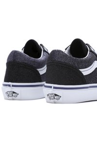 Zapatillas negras y brillantes con franjas blancas, que cuentan con un collar acolchado, parte superior texturizada y el logotipo característico de Vans en el talón.