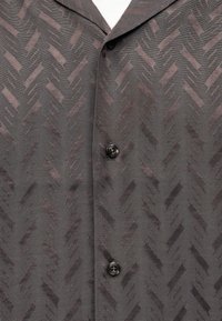 Σκούρο γκρι πουκάμισο με υφή γεωμετρικού μοτίβου και δύο μαύρα κουμπιά κλεισμένα κατά μήκος του εμπρόσθιου καβάλου.