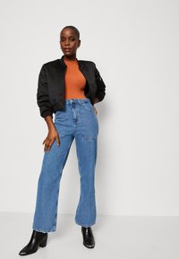 Svart bomberjacka, åtsittande brun topp, högmidjade blå vida jeans och svarta klackade ankelstövlar med en texturerad yta.