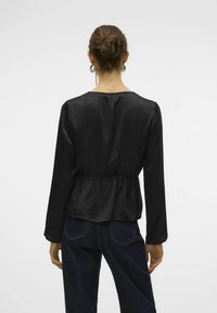 Sort langærmet bluse med en blød tekstur, peplum-talje og rund halsudskæring. Båret med mørke denimjeans. Vist fra ryggen.