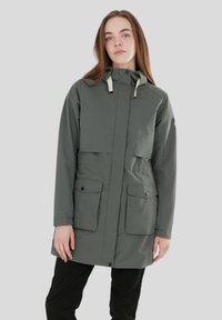 Giacca verde impermeabile con cappuccio, dotata di una patta frontale, due tasche laterali e cordini a contrasto, realizzata in tessuto liscio.