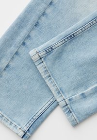 Close-up of light blue denim jeans showing detailed stitching along overlapping pant legs.