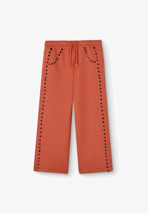 Zweetbroek in een roestoranje kleur, gemaakt van zacht materiaal. Heeft zwarte stippen aan de zijkant en twee voorzakken met een trekkoord in de taille.