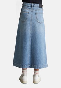 Hellblauer Jeansrock mit ausgestellt Design, knielang, ausgestattet mit zwei Gesäßtaschen und einem gesteppte Saum. Getragen mit weißen Turnschuhen und gemusterten Socken.