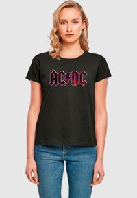 Black cotton t-shirt featuring red and black AC/DC logo design. Short sleeves, crew neck, and relaxed fit. Simple style, no patterns or accents.