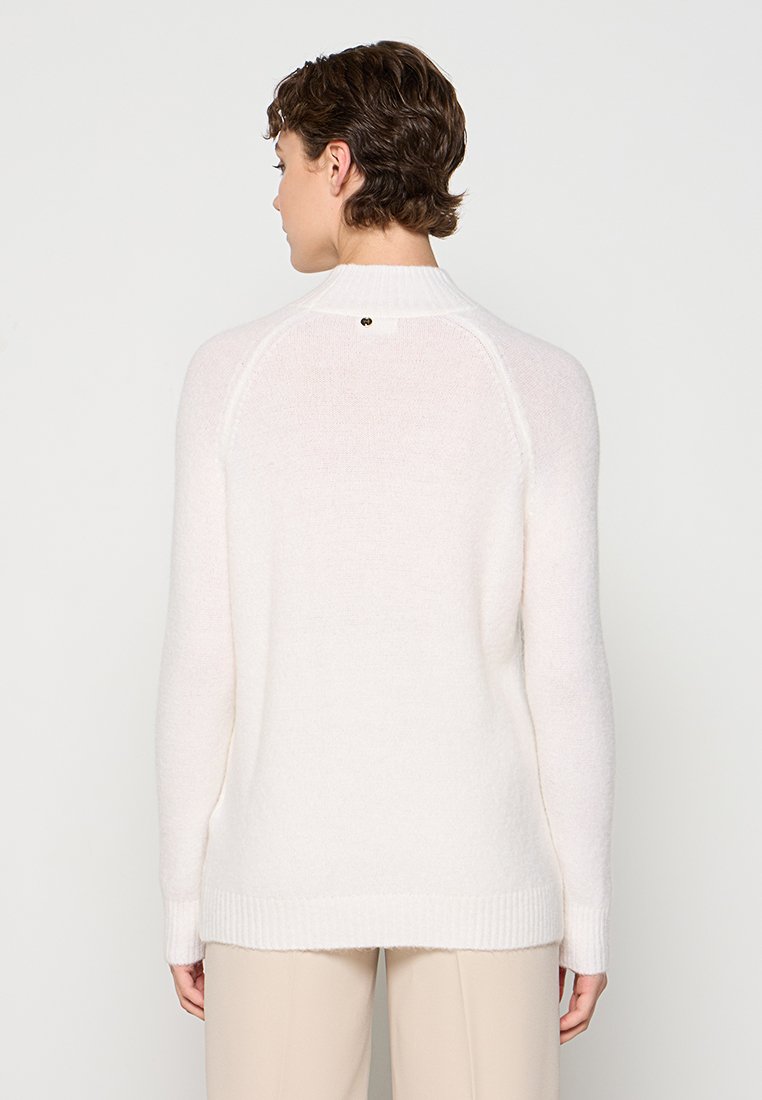 Jersey blanco de punto con dobladillo acanalado y mangas raglán. Presenta un pequeño detalle metálico en la parte posterior del cuello. Textura suave, corte holgado.
