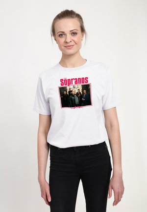 Kvinde iført en hvid T-shirt med et rødt "The Sopranos" logo og et printet gruppebillede fra tv-showet på forsiden.