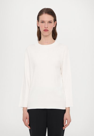 Maglione bianco a costine con scollo rotondo e maniche lunghe. Presenta un delicato motivo testurizzato, abbinato a pantaloni neri.