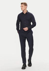 Camicia a maniche lunghe blu navy con colletto, abbinata a pantaloni su misura e scarpe eleganti nere lucide. Tessuto liscio, design elegante.