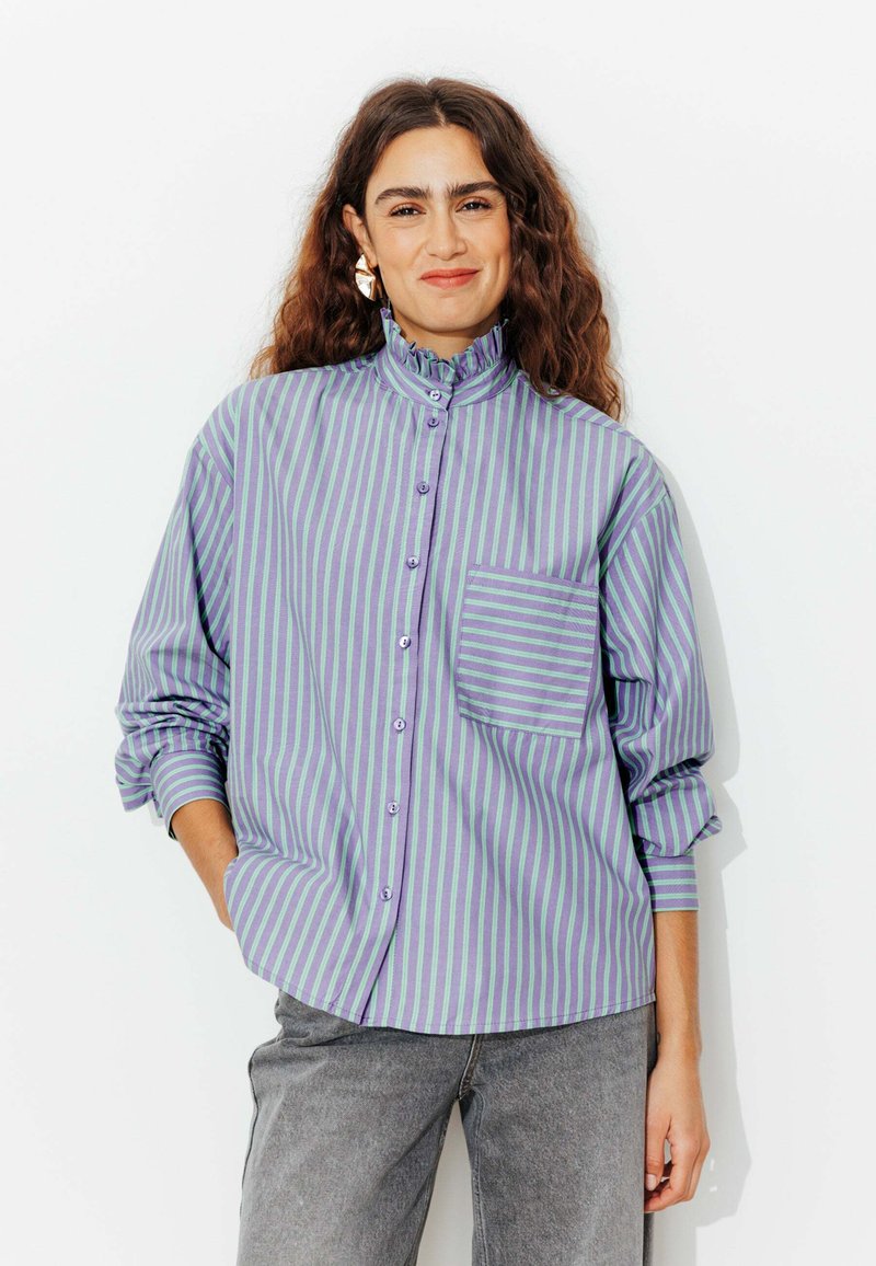 Chemise à rayures en violet et vert, avec un col froncé et une poche poitrine. Tissu doux avec une coupe décontractée.