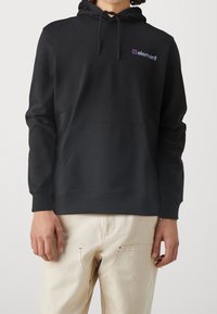 Sweat à capuche noir avec une poche kangourou, des poignets côtelés et un petit logo violet sur la poitrine. Fabriqué en tissu doux avec une texture lisse.