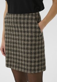Jupe en tweed avec un motif à carreaux noir et beige, longueur genou, avec des poches latérales et une finition texturée.