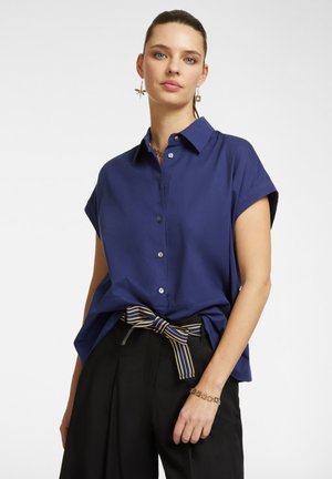 Navy blue short-sleeve button-up shirt with a collar; fabric is smooth with a relaxed fit. Paired with black trousers and a striped belt.