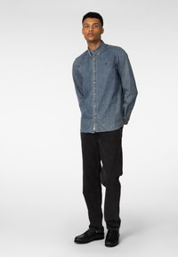 Mørkeblå denimskjorte med knapp-ned krage og lange ermer, kombinert med svarte jeans og svarte sko. Enkel, uformell design.