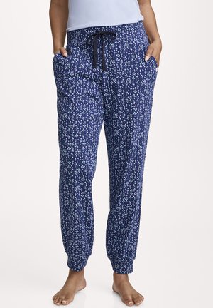 Woman wearing navy blue jogger pants with small light blue floral pattern and black drawstring, hands in pockets, barefoot.