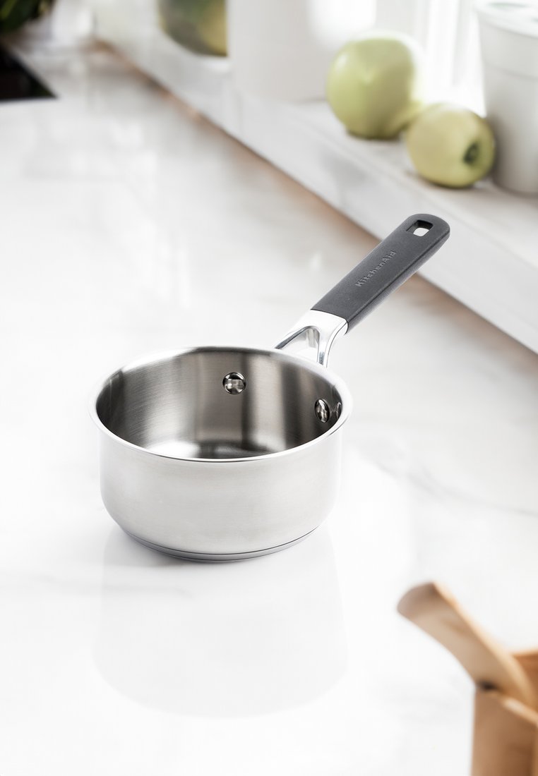 Nerezová oceľová panvica s elegantným strieborným povrchom, čiernou plastovou rukoväťou a dvoma nitmi upevňujúcimi rukoväť k hrncu.