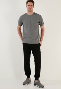 Tricou gri cu manșete scurte și decolteu rotund, asortat cu pantaloni jogger negri și adidași gri. Țesătură netedă, croială relaxată. Design simplu.