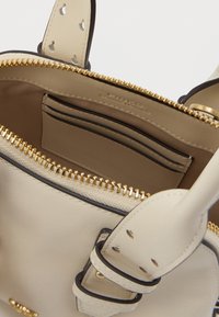 Interiér béžovej koženej kabelky s uzatváraním na zips, viacerými priehradkami na karty a detailmi zlatého kovania. Hladké textúry a čisté línie.