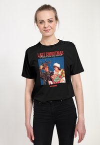 Černé bavlněné tričko s barevným grafikem zobrazujícím dva slavnostní postavy, nad obrázkem červený nápis "LAST CHRISTMAS".