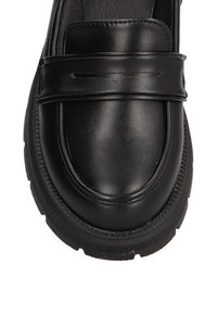 Mocasines de cuero negro con acabado suave, que presentan un acento de costura elevada en la parte superior y una suela de goma texturizada.