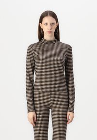 Langsleeve top en bijpassende leggings in een beige en zwarte houndstooth patroon. Glad, rekbaar materiaal met een hoge halsontwerp.