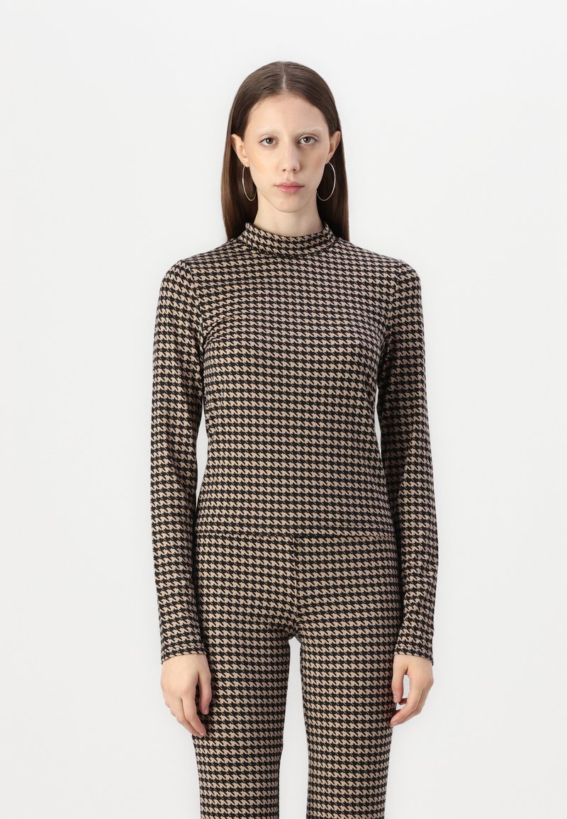 Langsleeve top en bijpassende leggings in een beige en zwarte houndstooth patroon. Glad, rekbaar materiaal met een hoge halsontwerp.