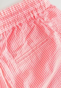 Roza prugasta tkanina s nježnom teksturom, koja sadrži elastični pojas i detalj stražnjeg džepa, naglašavajući tanke bijele i ružičaste pruge.