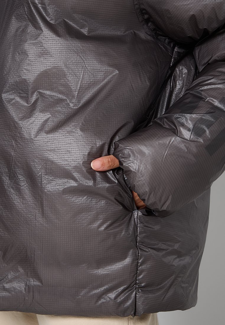 Giacca a vento grigia con superficie testurizzata, dotata di colletto alto, chiusura con zip e tasche laterali, che enfatizza calore e isolamento.