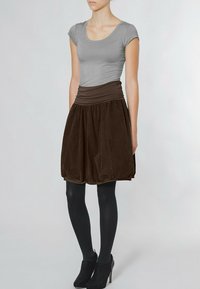 Graues, eng anliegendes T-Shirt kombiniert mit einem dunkelbraunen Cord-Röckchen im Bubble-Stil. Der Rock hat einen breiten Taillenbund und eine geraffte Textur am Saum.