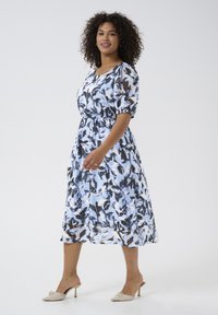 Light blue dress with black and white abstract patterns, short puff sleeves, elastic waist, and flowing midi length. Worn with nude kitten heels.