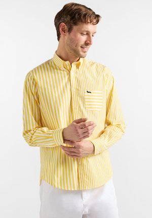 Camisa de manga larga con rayas amarillas y blancas, cuello abotonado, un pequeño bolsillo en el pecho y un detalle de logo en negro.
