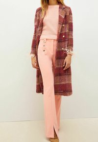 Śliwkowy p�łaszcz w kratę z wełny z złotymi guzikami; różowy sweter z prążkowanej dzianiny; dopasowane różowe spodnie z guzikowymi akcentami; eleganckie obuwie.
