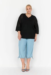 Črn oversized top z v-izrezom in kratkimi rokavi, v kombinaciji s svetlo modrimi krajšanimi hlačami z nastavljivimi vrvicami na robu.