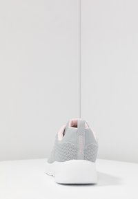 Zapatillas de malla gris con un acabado texturizado, detalles en rosa y una suela blanca. La vista trasera muestra una lengüeta y un detalle del logo.