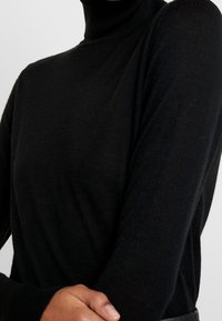 Schwarzer Rollkragenpullover mit langen Ärmeln, aus einem feinen Strickmaterial gefertigt. Verfügt über einen enganliegenden Kragen und eine weiche Textur.