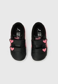 Παιδικά πάνινα παπούτσια Puma σε μαύρο και ροζ χρώμα με δύο ροζ λουράκια σε σχήμα καρδιάς σε κάθε παπούτσι, φωτογραφημένα από πάνω σε λευκό φόντο.