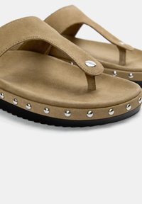 Svetlozeleni semafor flip-flop sandali iz nubuk antilopa s kovinskimi poudarki na črnem gumijastem podplatu. Pasovi se ponašajo z minimalističnim oblikovanjem in gladko teksturo.