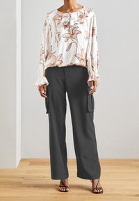 Blusa bianca a fantasia floreale con colletto e maniche arricciate, abbinata a pantaloni cargo neri a gamba larga con tasche laterali e finitura liscia.