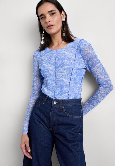 Απαλό μπλε μπλουζάκι με μακρύ μανίκι και μοτίβο ροζ, διαφανής υφή, συνδυασμένο με ψηλόμεσα σκούρα τζιν παντελόνια που διαθέτουν κλασικό σχέδιο πέντε τσέπης.